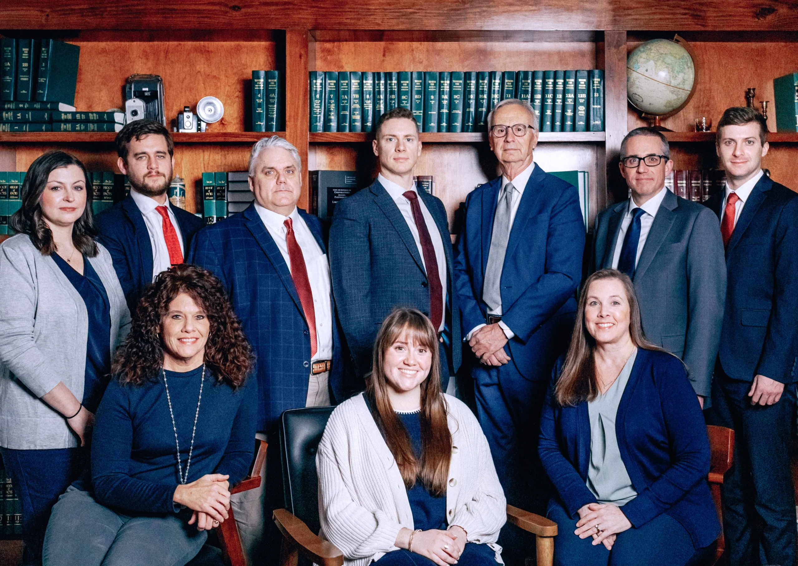 A professional group portrait of the ten team members of The Crabtree Law Firm. Three women are seated in the foreground with seven men standing behind them, in front of a wall of law books in an office library.